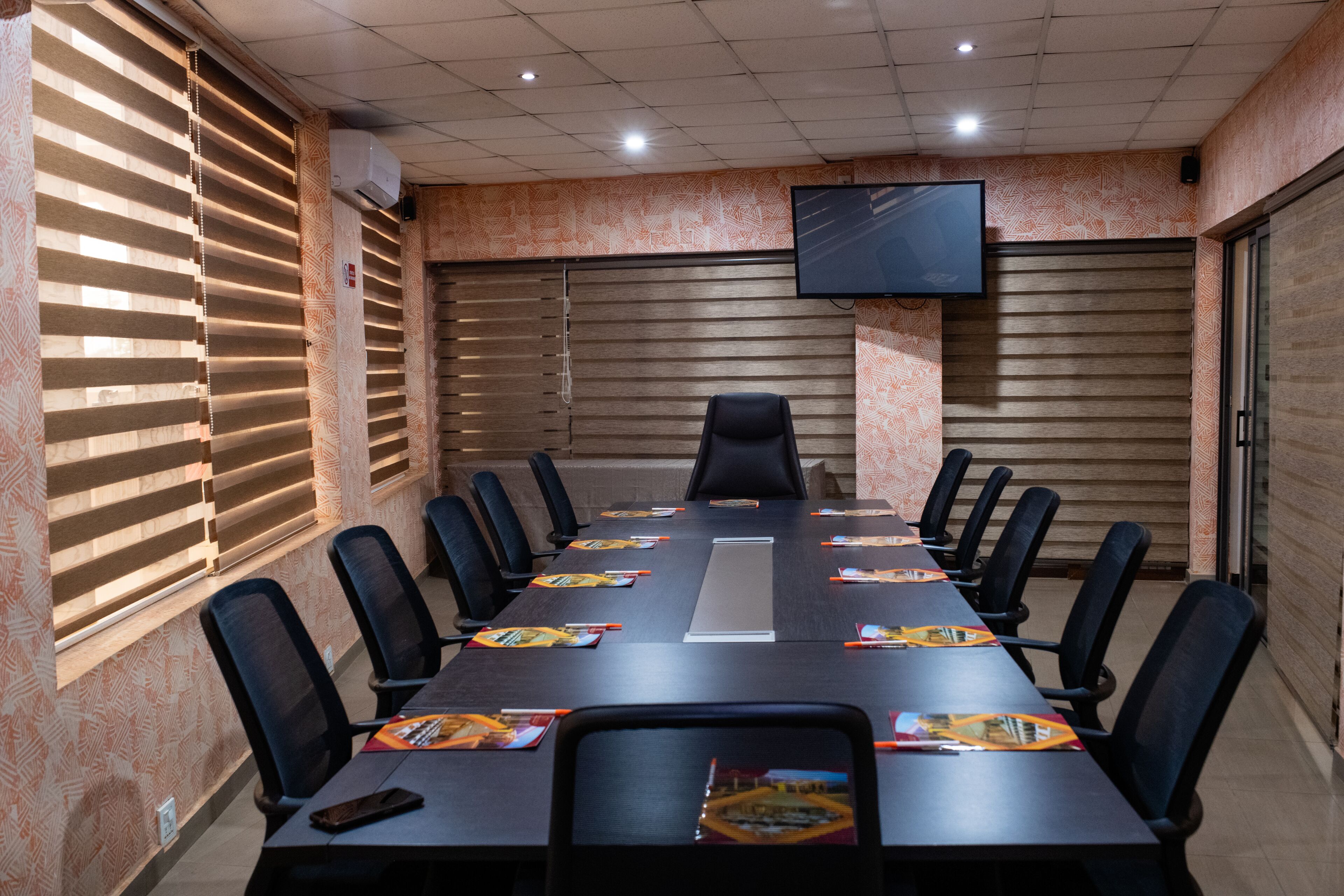 A conference room with a long table, black chairs, and a TV mounted on the wall.