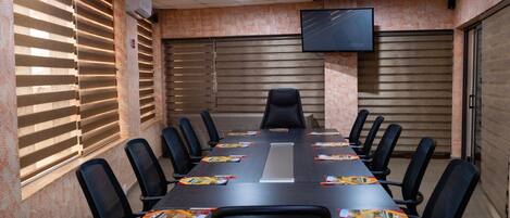 A conference room with a long table, black chairs, and a TV mounted on the wall.