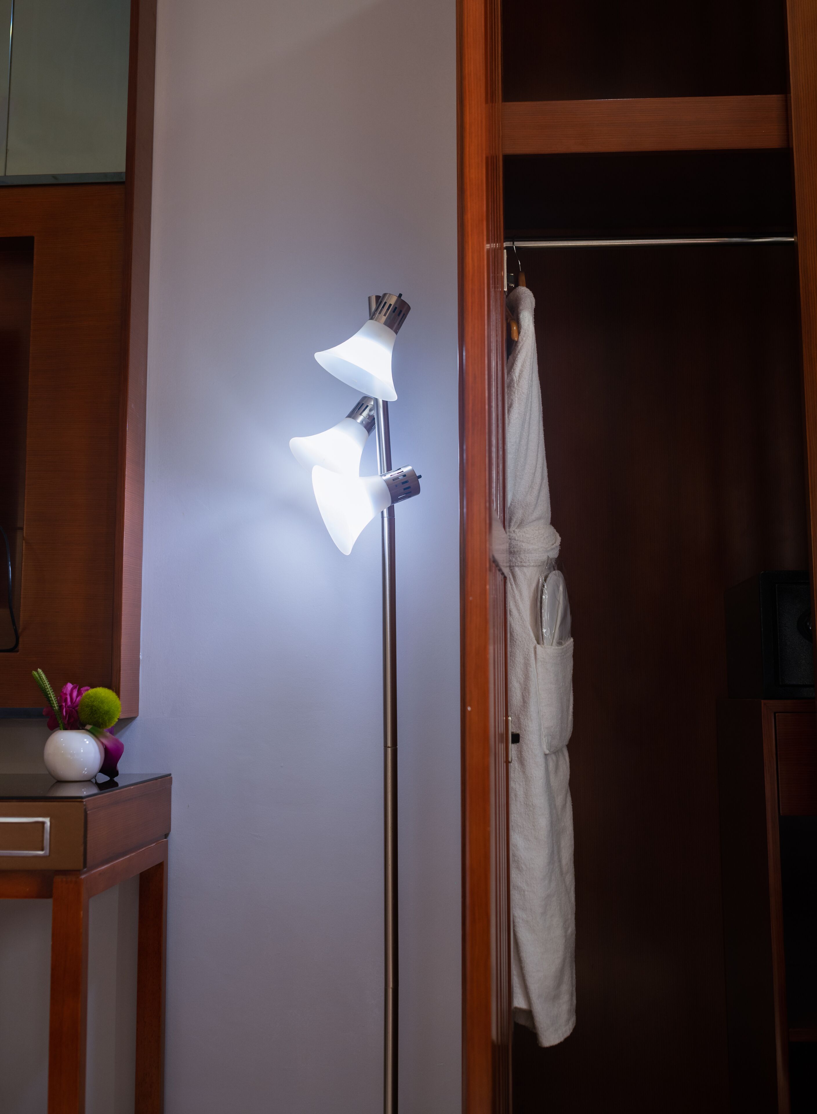 A bathroom with a wooden vanity, a white vase with a green plant, and a towel hanging on a rack.