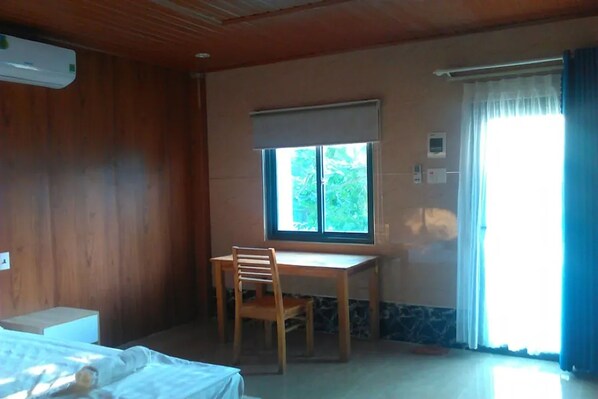A room with a bed, a desk, and a chair. There is a window with a view of greenery outside.