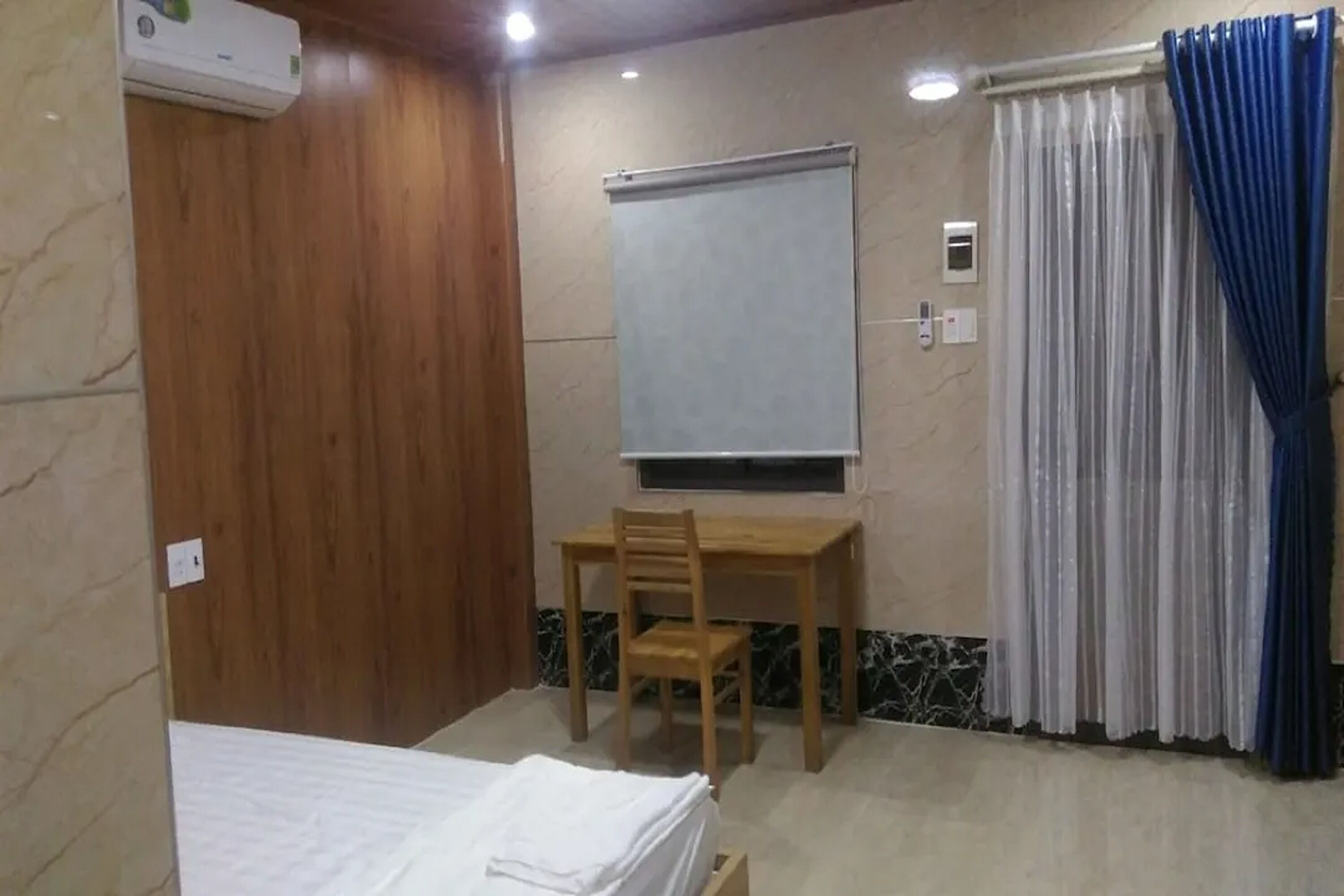 Una habitación con una cama, un escritorio de madera con silla, un televisor y una ventana con cortinas.