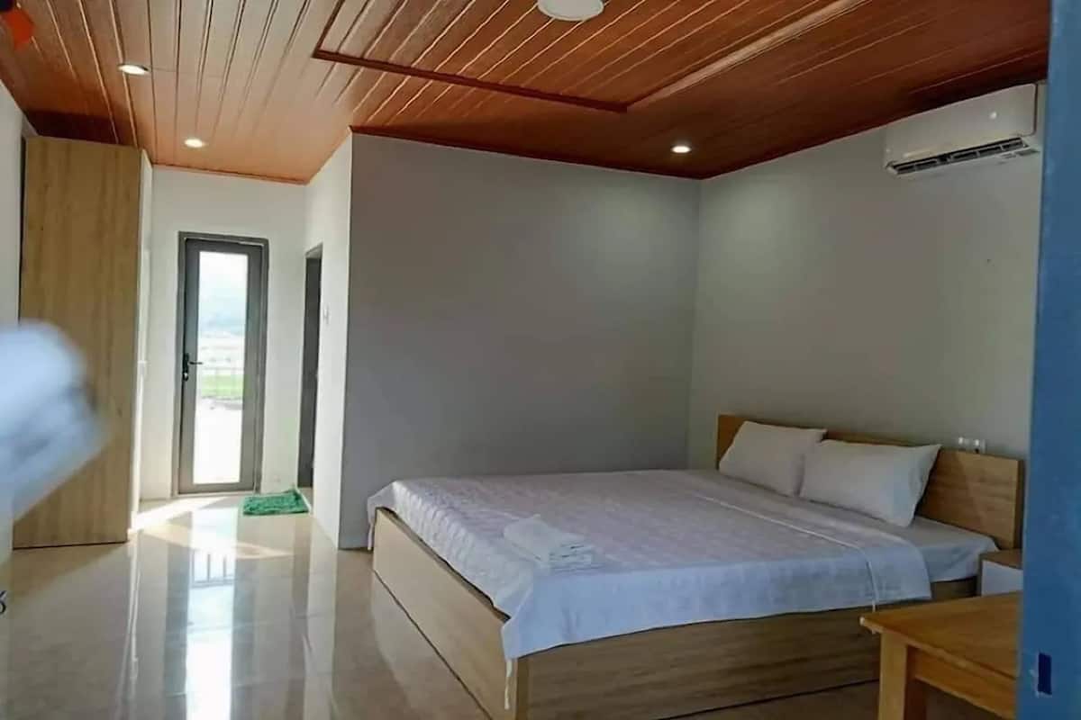 Une chambre moderne avec un plafond en bois, un grand lit recouvert de draps blancs et une table de chevet en bois.