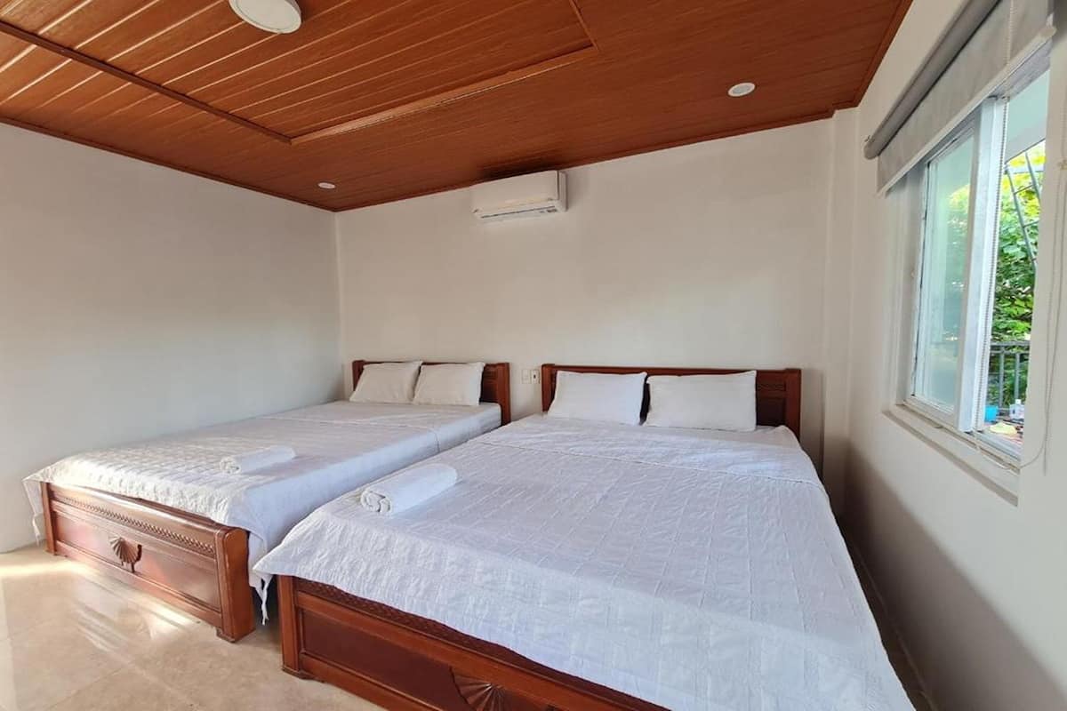Une chambre avec deux lits en bois, du linge de lit blanc, un plafond en bois et une fenêtre donnant sur un paysage verdoyant.