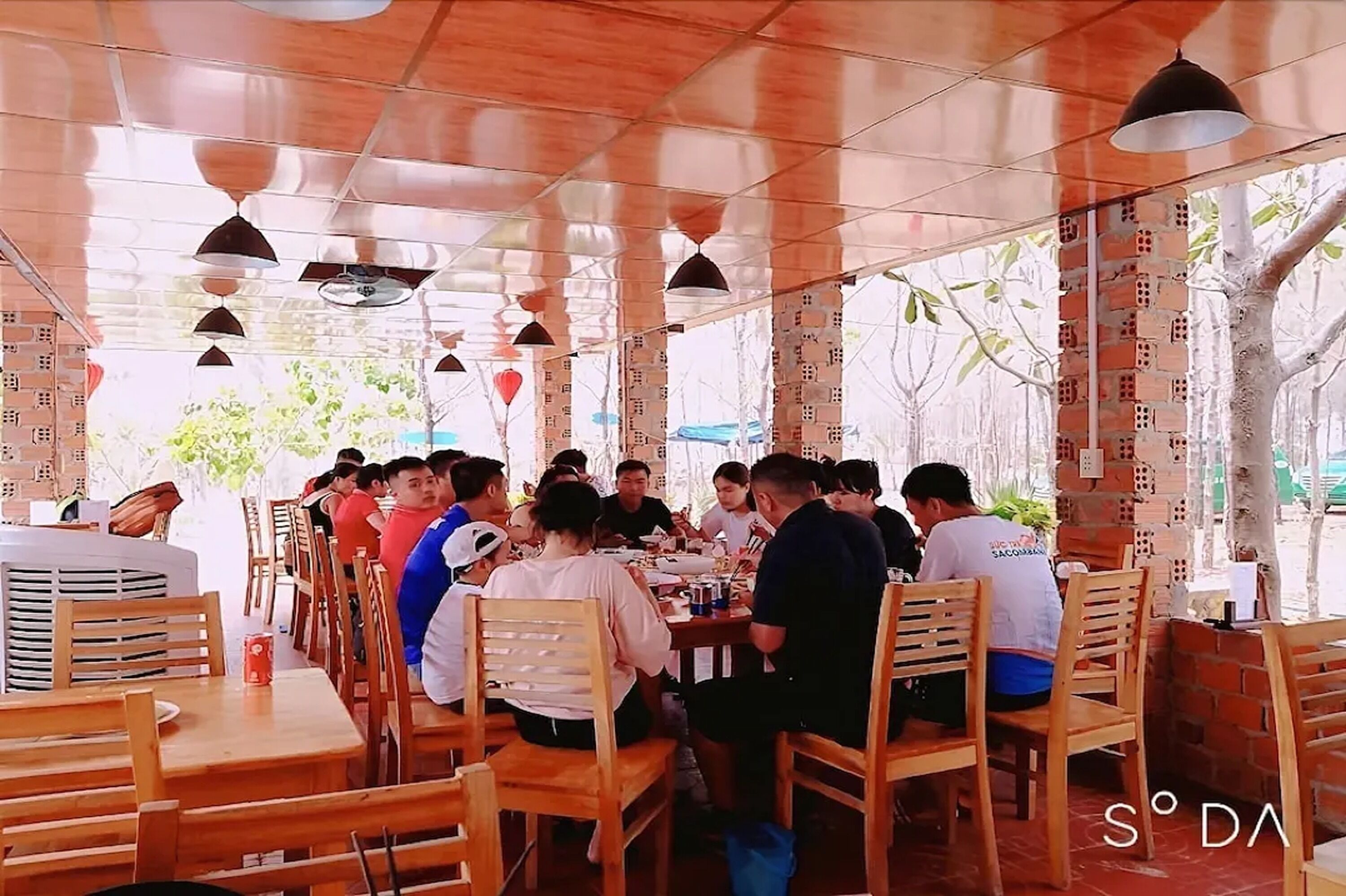A restaurant with wooden tables and chairs, brick walls, and hanging pendant lights.