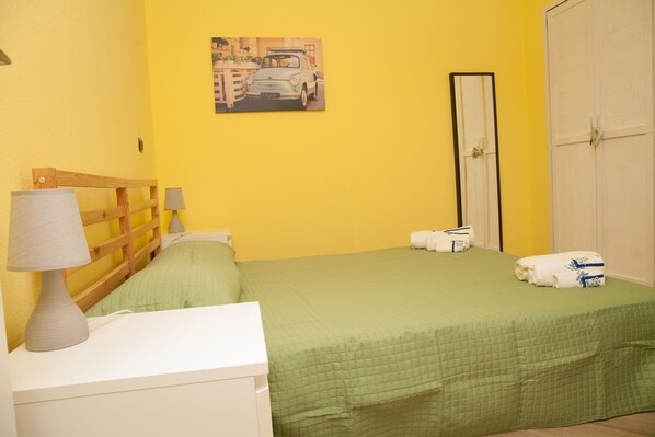 Une chambre avec un lit, une table de chevet avec une lampe, un tableau au mur et une armoire.