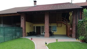 A building with a covered patio area, brick columns, and a staircase leading to an upper level.