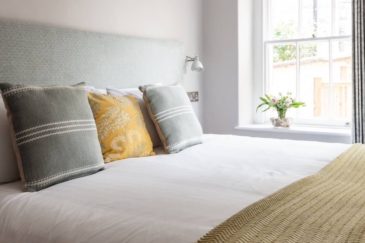 A bedroom with a bed, pillows, a bedside lamp, and a window with a view of the outside.