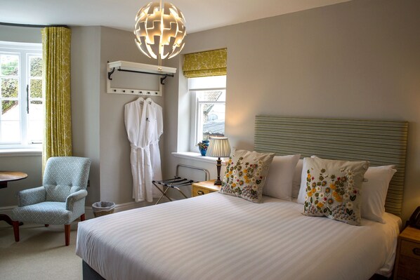 A neatly arranged bedroom with a large bed, a chair, a drying rack, and a window with curtains.