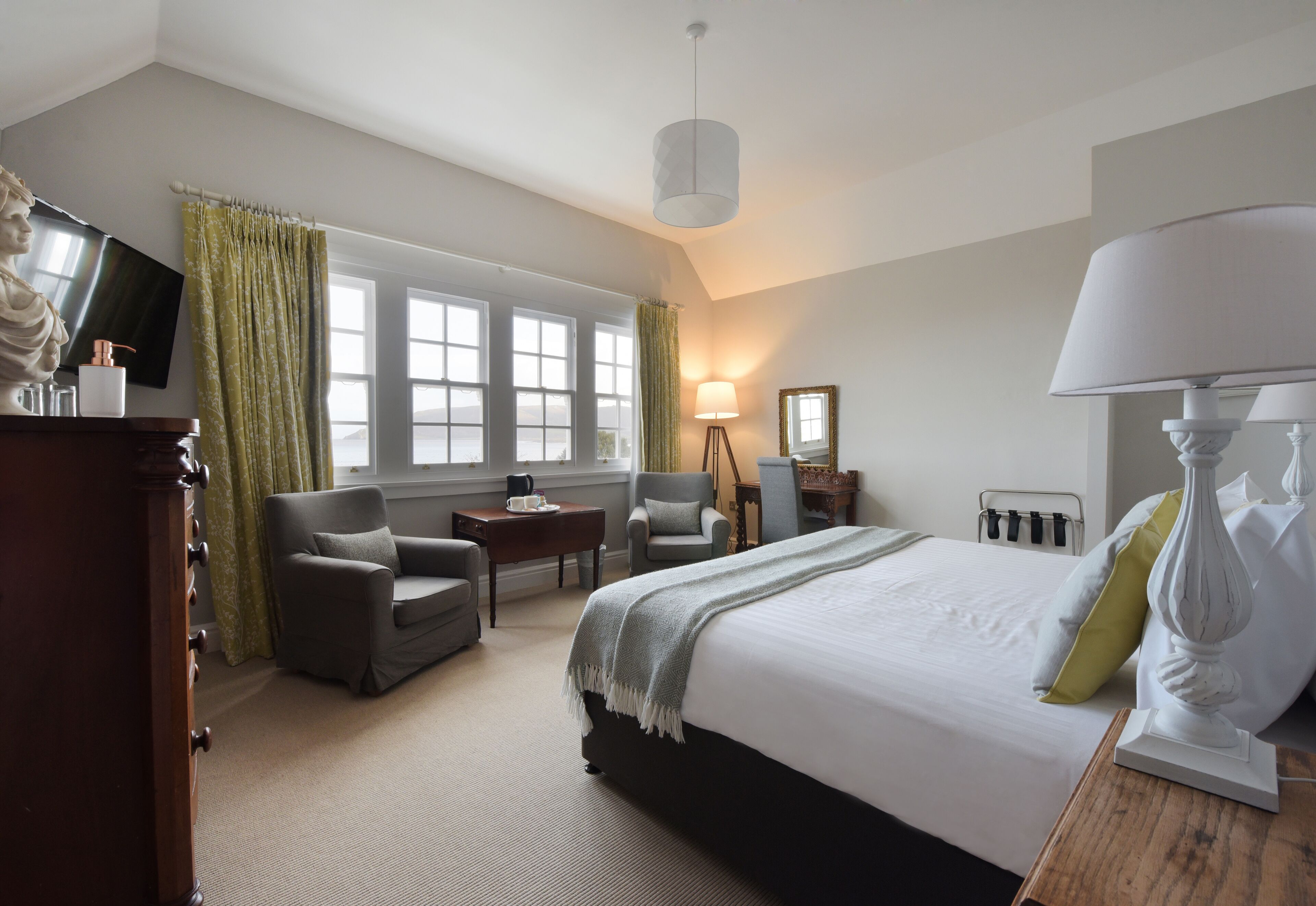 A hotel room with a large bed, two armchairs, a desk, a lamp, and a television.