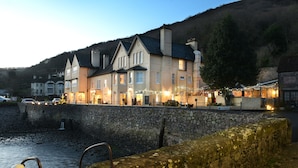 Un hôtel situé au bord de l’eau, avec des murs en pierre, de nombreuses fenêtres et des guirlandes lumineuses.