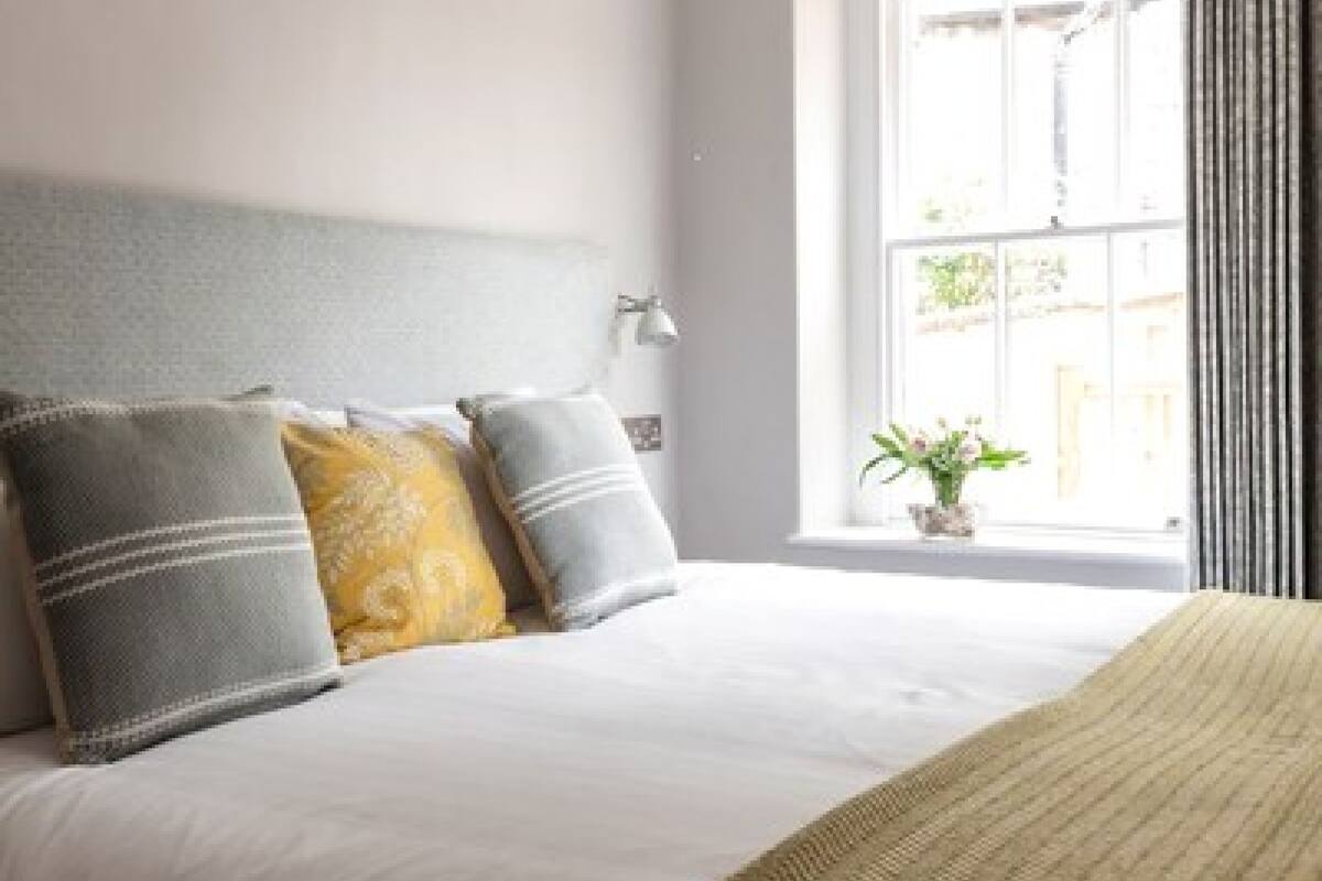 A neatly made bed with a patterned throw, a bedside lamp, and a window with curtains.