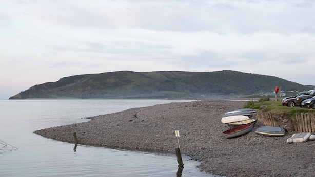 Un rivage rocheux où sont amarrés des bateaux et où sont garées des voitures, près de l’eau.
