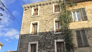 Un edifici de pedra de diverses plantes, amb diverses finestres, algunes amb persianes, i un balcó.