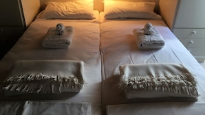 Un llit doble amb dues almoines, dues tovelloles doblegades i una taula de nit amb una làmpada.