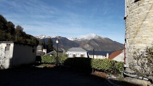 Une vue de rue avec un bâtiment en pierre, un petit abri de jardin et une montagne en arrière-plan.