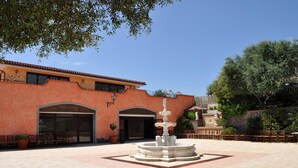 Un patio con una fuente, mobiliario exterior y un edificio con puertas arqueadas.