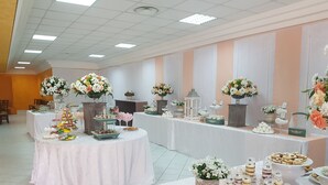 Un salón de banquetes con varias mesas redondas cubiertas con manteles blancos, decoradas con arreglos florales y diversos alimentos.