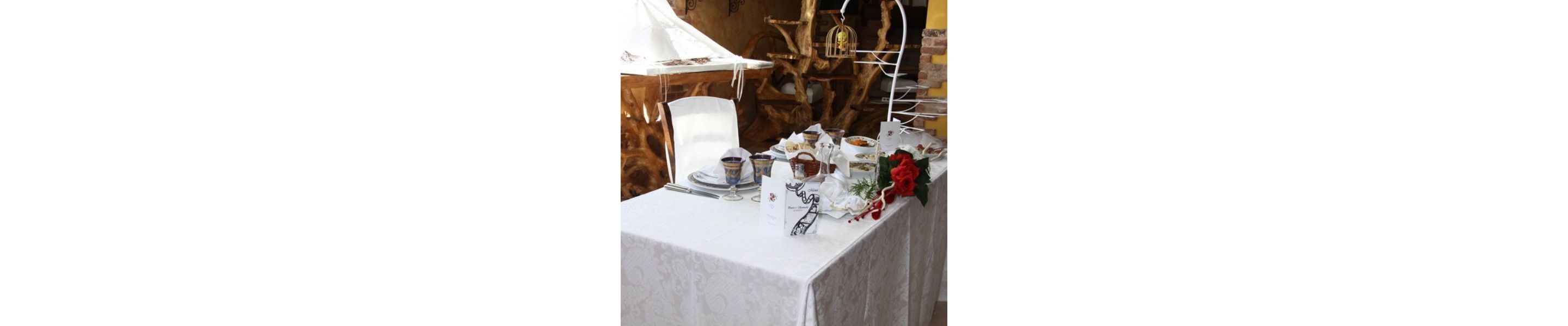 Een gedekte tafel met een witte tafeldoek, borden, glazen en een menukaart.