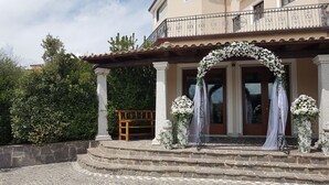 Un edificio con un acceso adoquinado de piedra, un banco de madera y un arco decorado con flores.