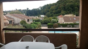 Ein Balkon mit Tisch und Stühlen, der auf einen Wohnbereich mit Häusern und einem Schwimmbad blickt.