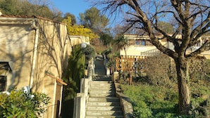 Eine steinerne Treppe führt zu einem Gebäude mit einem Ziegeldach, umgeben von Grünpflanzen und Bäumen.