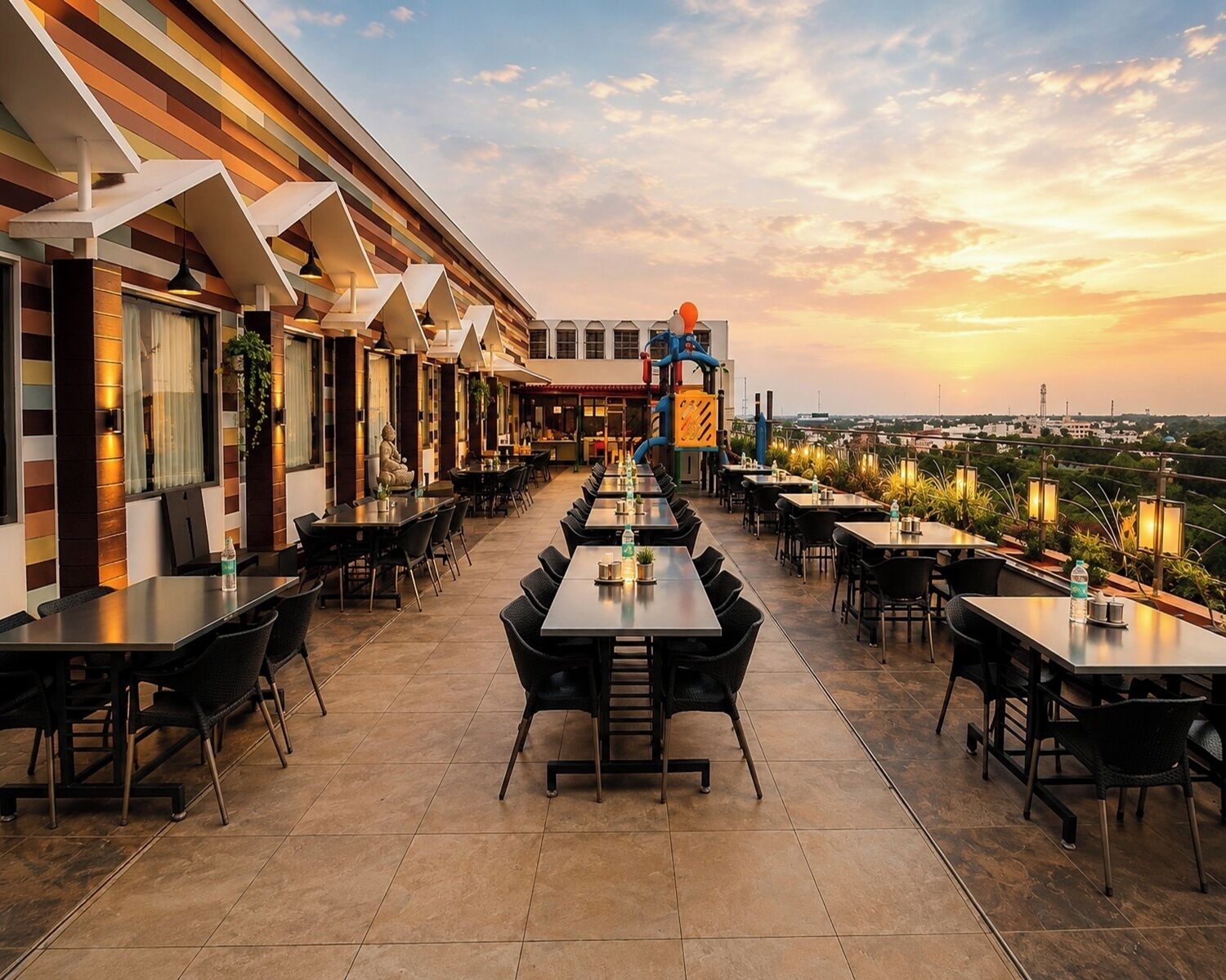 Ein Dachrestaurant mit mehreren Tischen und Stühlen, Blick auf die Stadt und einem Sonnenuntergang im Hintergrund.