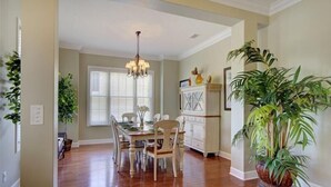 Un comedor con una mesa y sillas de madera, una araña y plantas en macetas.