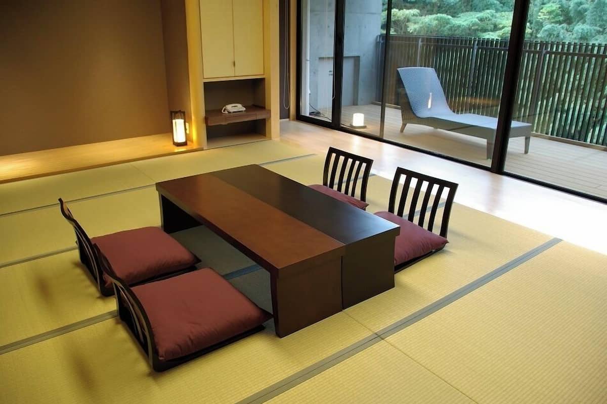 A tatami mat room with a low table, chairs, and a view of a balcony with a chair.
