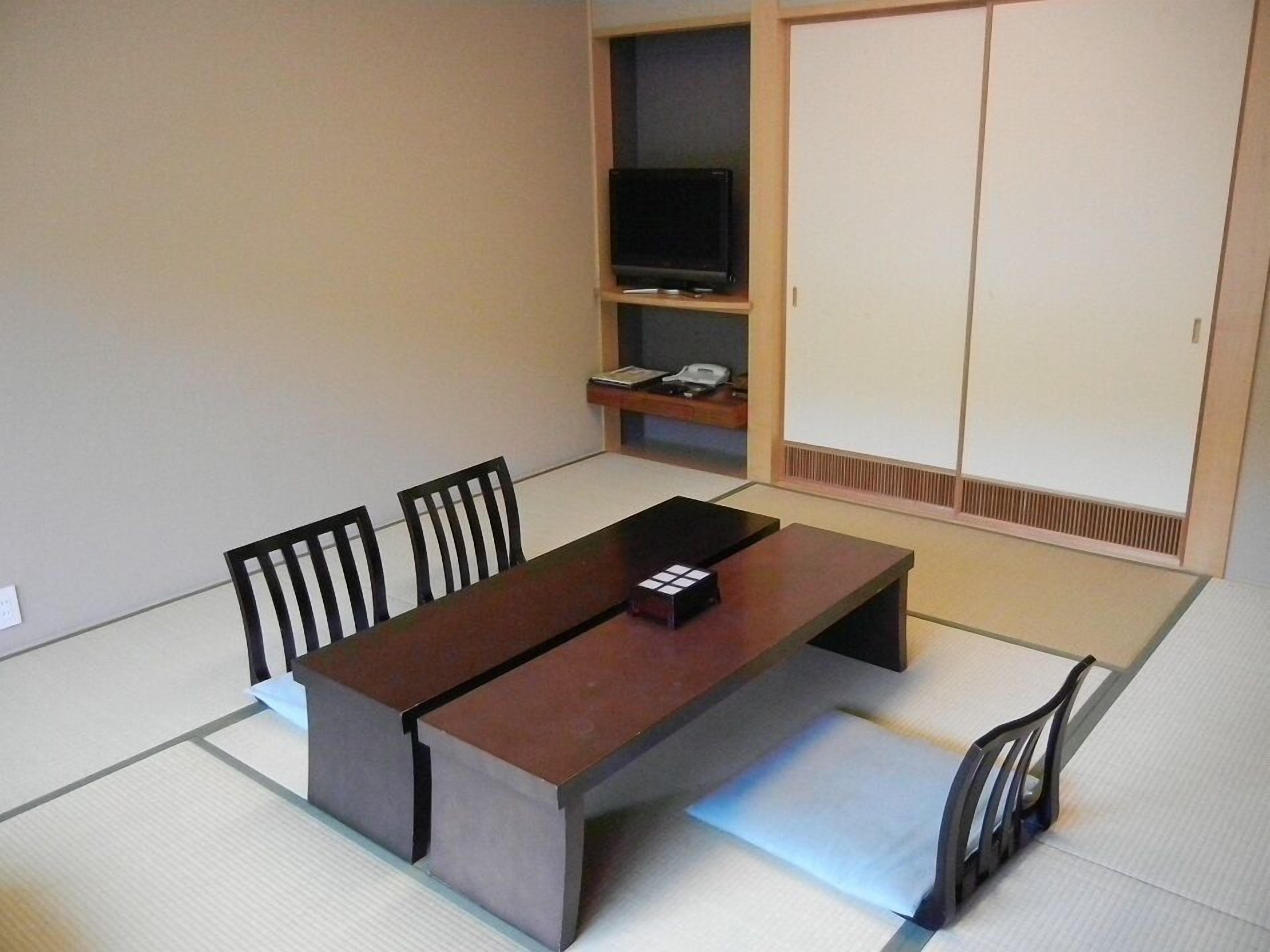 Una habitación de estilo japonés tradicional con suelo de tatami, una mesa baja con control remoto, un televisor en un estante y puertas correderas.