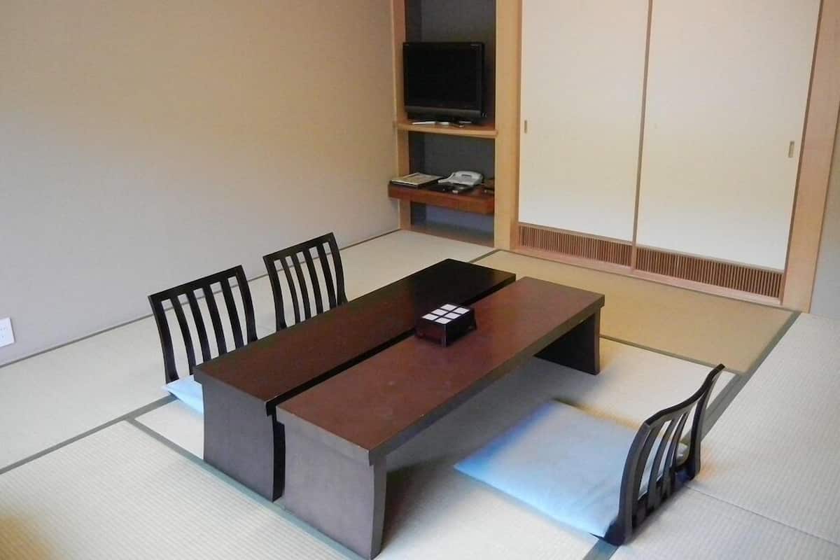 A traditional Japanese-style room with tatami flooring, a low table with a remote control, a television on a shelf, and sliding doors.