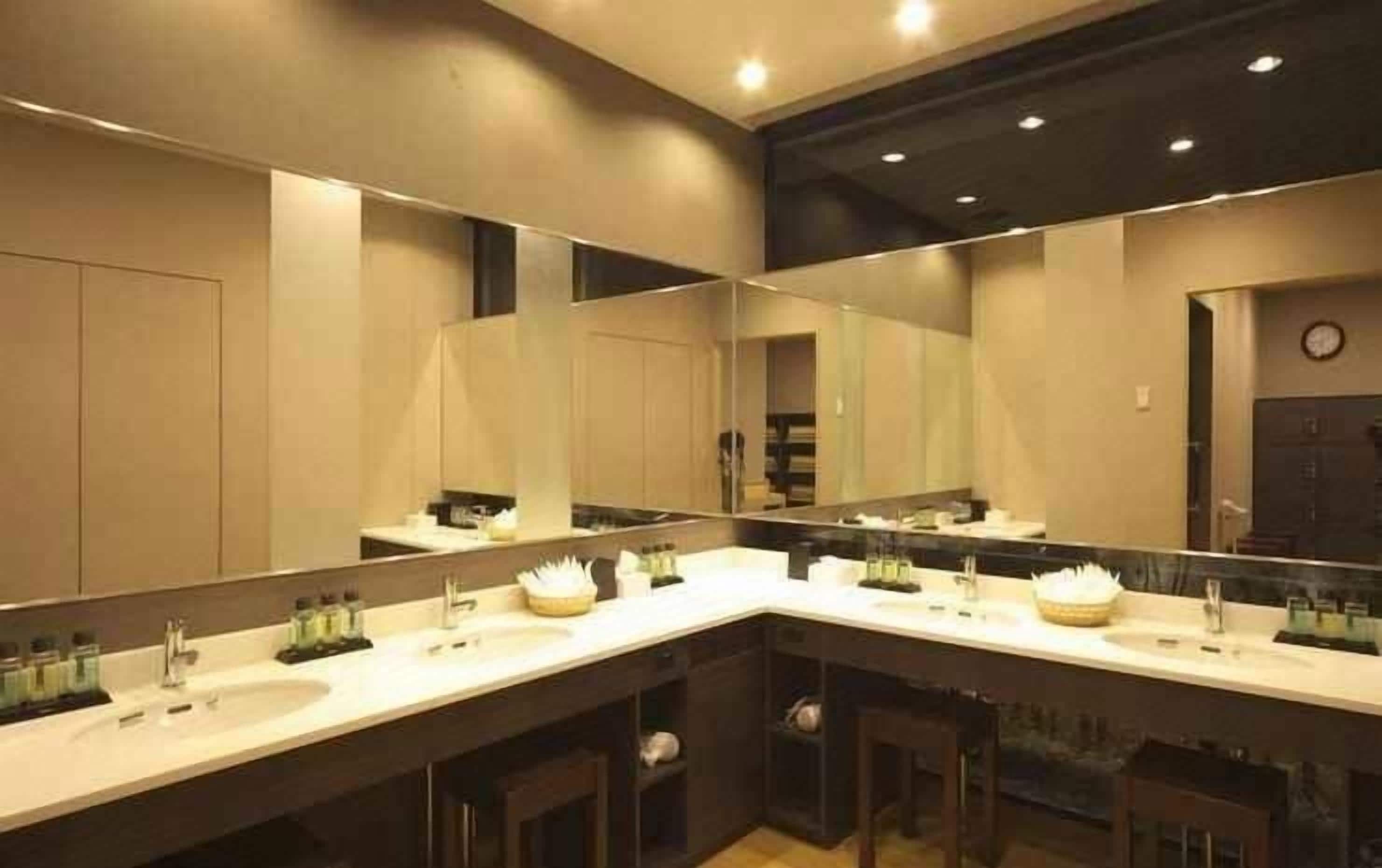 A modern bathroom with three sinks, large mirrors, and a clock on the wall.