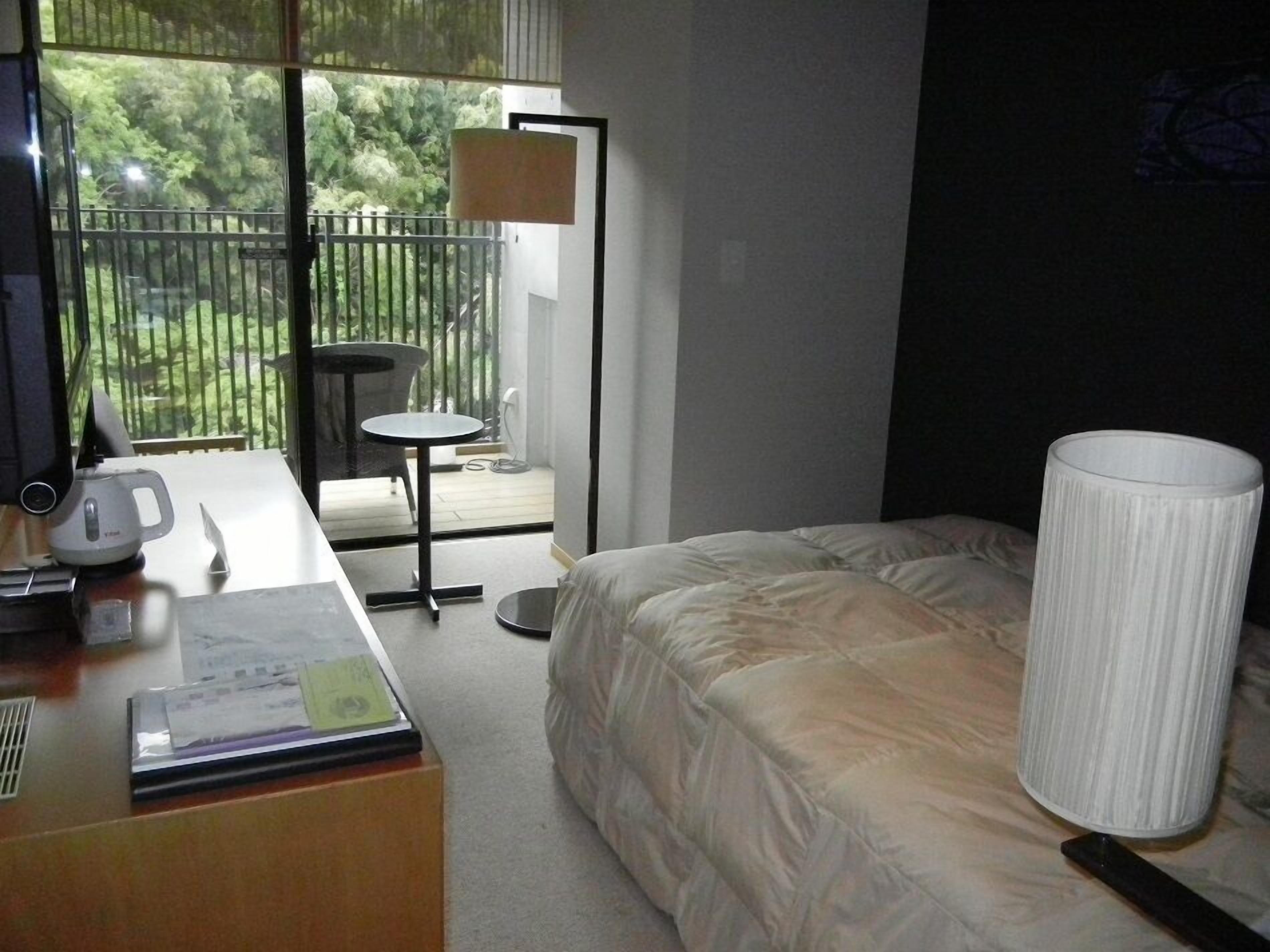 Habitación de hotel con cama, escritorio con lámpara, una silla y vista al exterior.