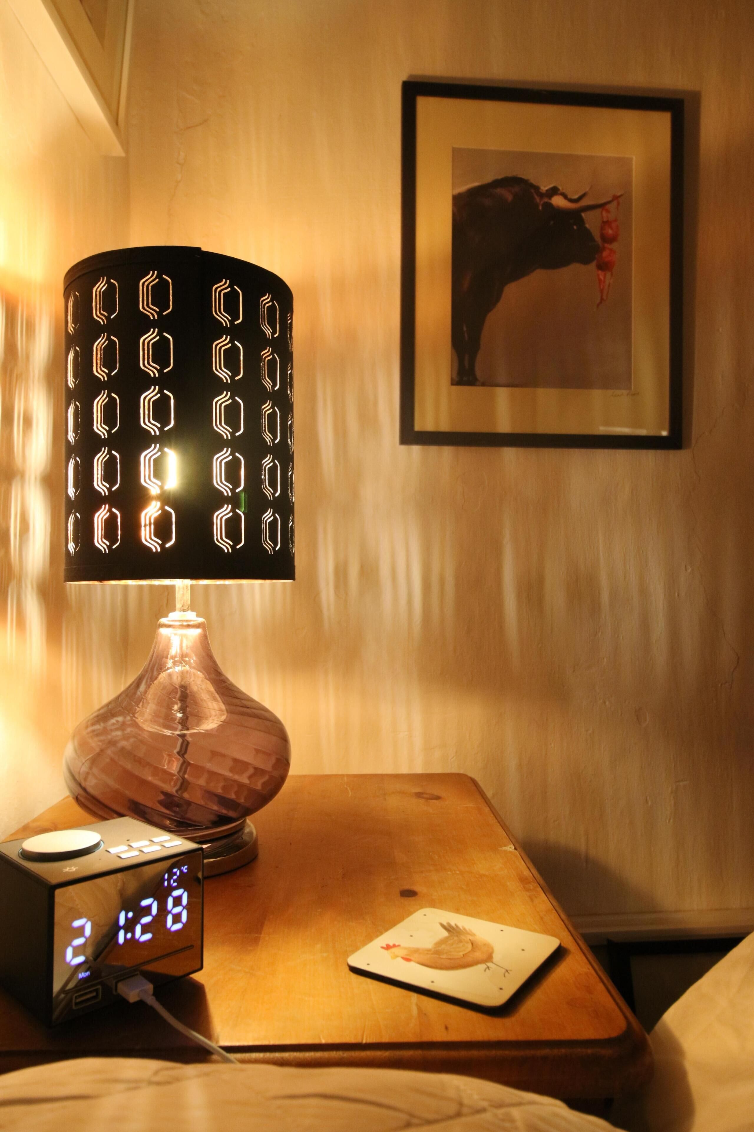 A bedside table with a digital clock, a lamp, and a framed picture on the wall.