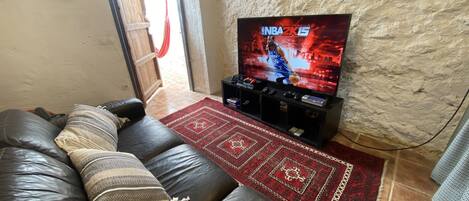 A living room with a leather sofa, a red patterned rug, a TV displaying NBA 2K15, and a dartboard on the wall.