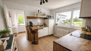 A modern kitchen with wooden flooring, white cabinetry, a central island with stools, a built-in microwave, and a view of the outside through large windows.