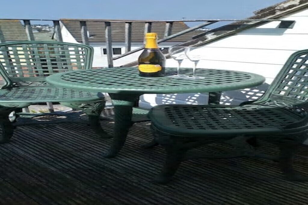 Une table et des chaises en métal vert sur un balcon, avec une bouteille et deux verres.