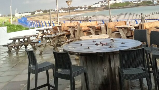 Een terras met tafels en stoelen, uitzicht op zee en een regenboog aan de hemel.