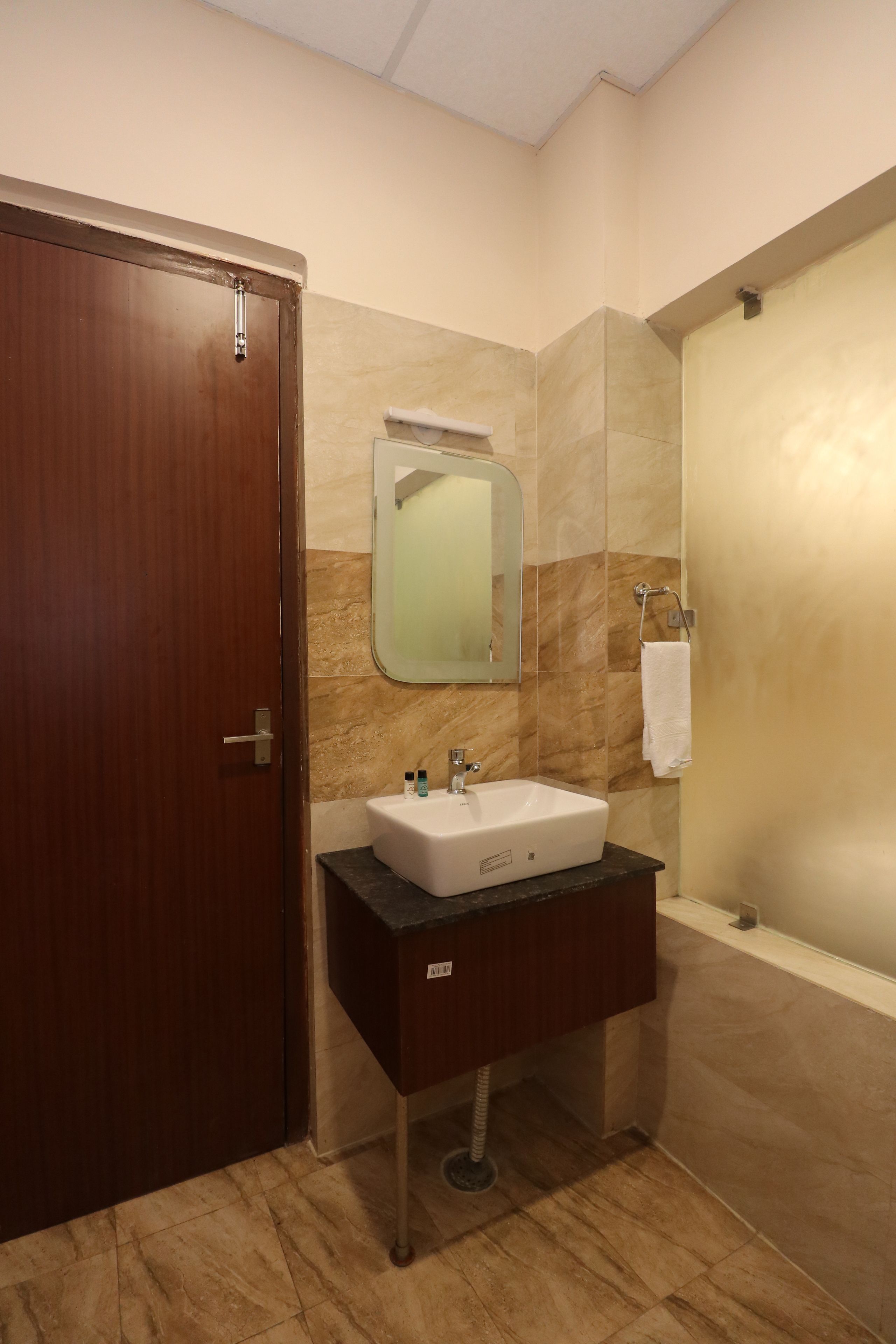 A bathroom with a wooden door, a white sink with a mirror above it, and a shower area.