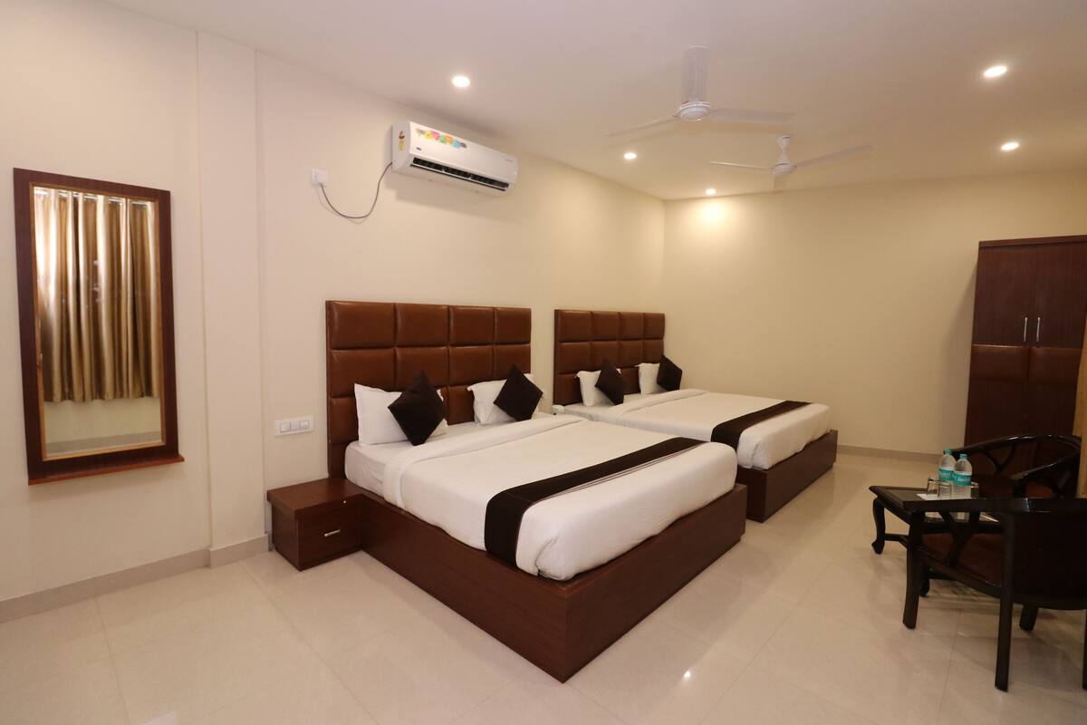 A hotel room with two beds, a desk, a chair, an air conditioning unit, and a ceiling fan.