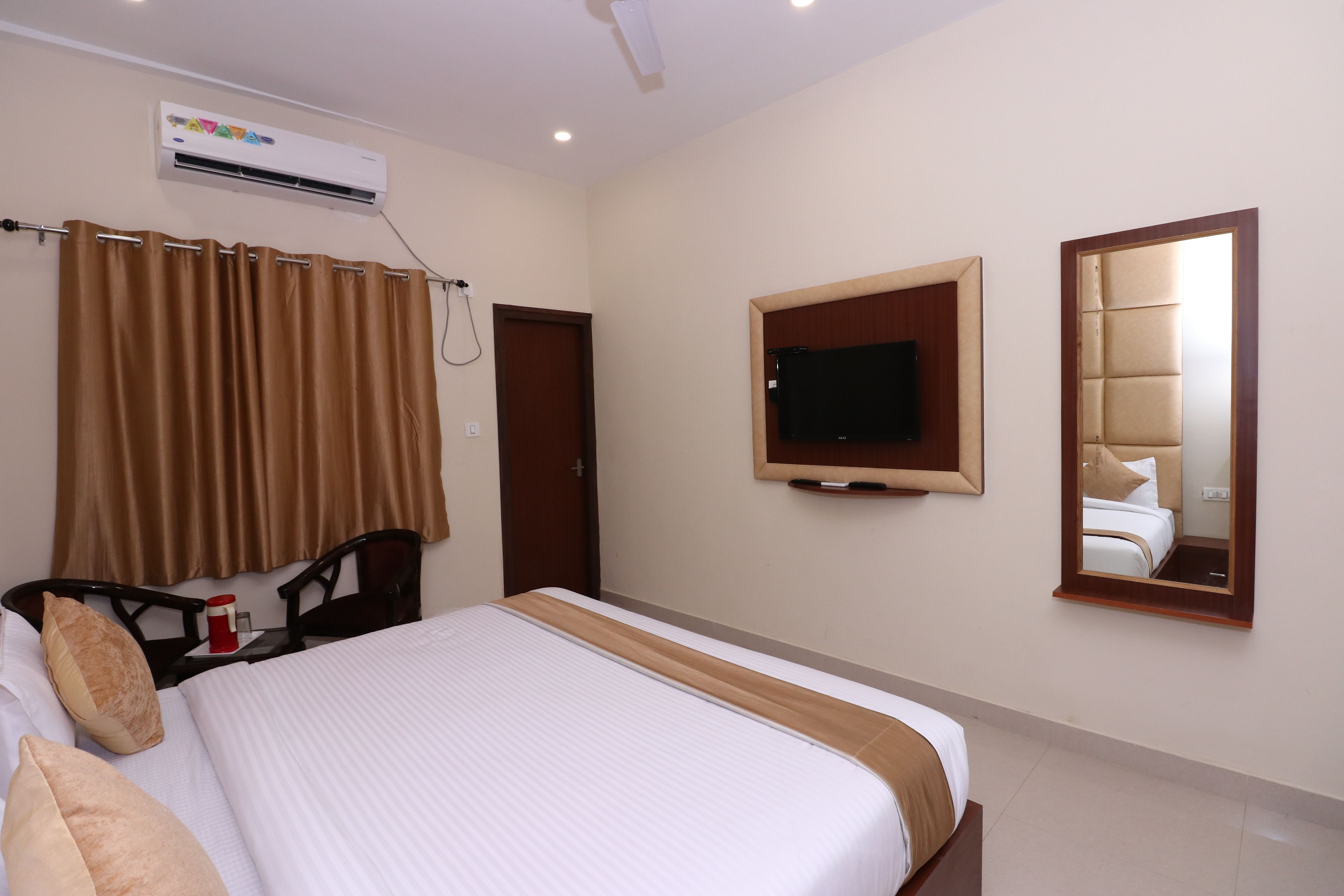 Habitación de hotel con cama, televisor montado en la pared, aire acondicionado y espejo.