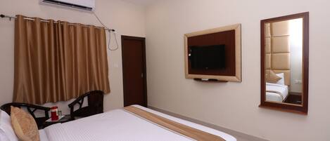 Habitación de hotel con cama, televisor montado en la pared, aire acondicionado y espejo.