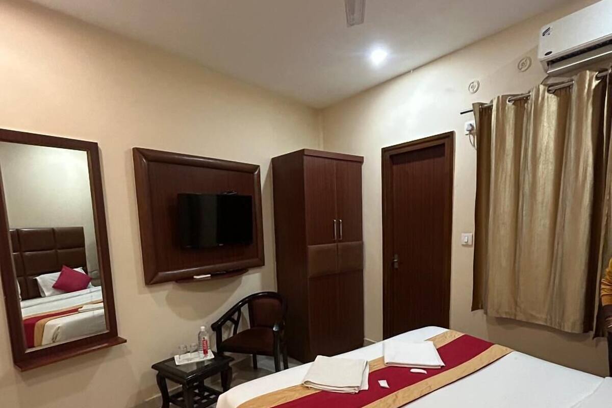 A hotel room with a bed, a desk, a chair, a TV mounted on the wall, and a ceiling fan.
