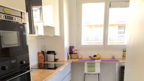 Una cocina compacta con horno negro, armarios blancos y un ventanal pequeño.