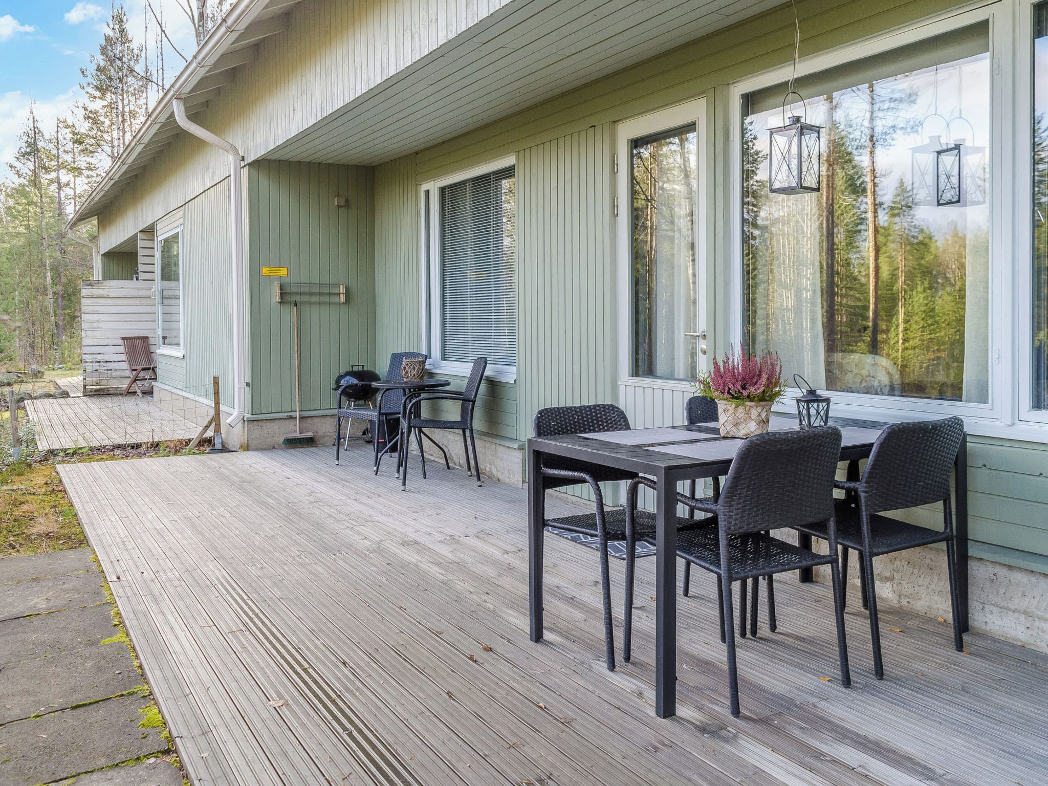 A covered outdoor area with a table and chairs, a grill, and a window with a view of trees.