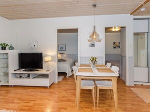 A modern living room with a flat-screen TV, a dining table with chairs, and a wooden ceiling.