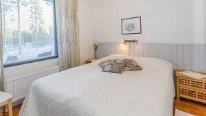 A bedroom with a large bed, a window with blinds, a bedside table with a lamp, and a framed picture on the wall.
