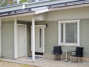 A single-story building with a covered porch, two chairs, and a window with blinds.
