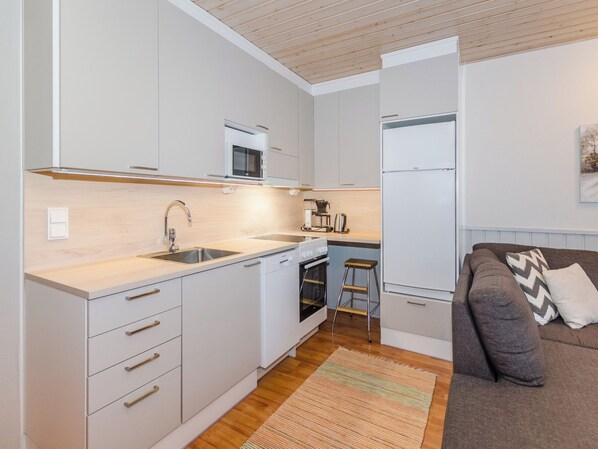 A compact kitchen with white cabinets, a stainless steel sink, a microwave, an oven, and a refrigerator.