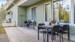 A covered outdoor patio with a table and chairs, a potted plant, and a view of the surrounding forest.