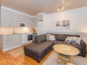 A modern kitchen with white cabinets, a microwave, and a stove. There is a gray sofa with a round coffee table and a painting on the wall.